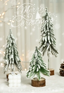Frosted pine Christmas trees with wooden bases and white bubble candle on desk