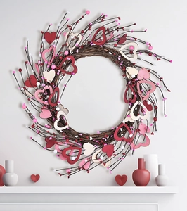 Detail view of heart-shaped twig wreath with wooden hearts and red berries on white wall