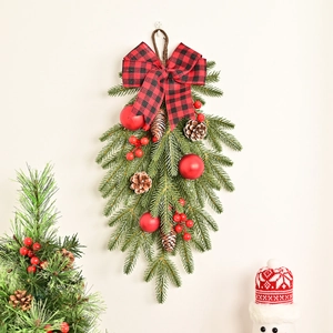Christmas pine needle teardrop swag with red berries and buffalo plaid bow hanging on wall