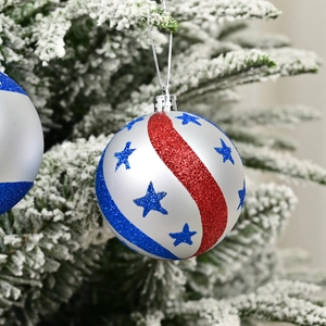 Patriotic Christmas ball ornament with red and blue stripes on snowy pine tree branch