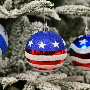 American flag Christmas ball ornament with blue stars and red white stripes on snowy tree