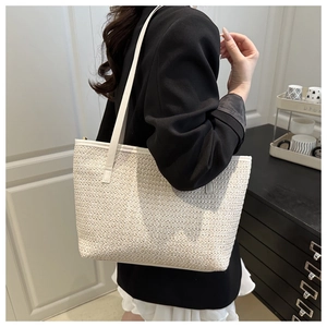 Close-up of cream woven tote bag with white leather straps worn on shoulder
