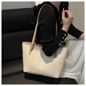 Detail of a beige woven tote bag with brown leather straps worn on a shoulder