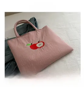 Close-up of pink nylon tote bag featuring red apple embroidery and fabric texture detail