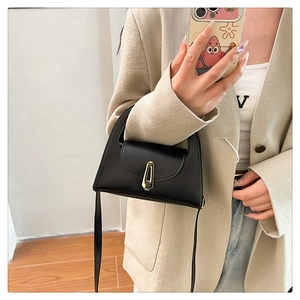 Detail of a minimalist black leather crossbody bag with a gold geometric metal buckle
