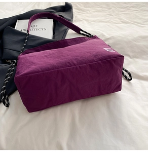 Detail of purple nylon tote bag with side embroidery and padded strap on white sheets