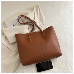 Detailed side view of brown tote bag with metal feet on white blazer background