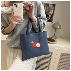 Close-up of red apple embroidery on a navy blue nylon tote bag with matte texture