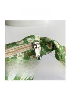 Detail of green daisy floral fabric and silver metal zipper closure on a handbag