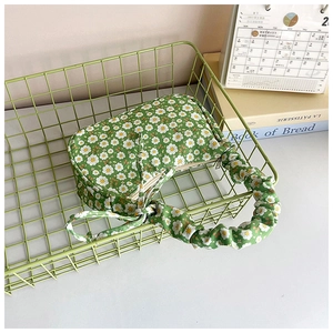 Detail of green floral handbag with ruched handles and daisy print in a basket