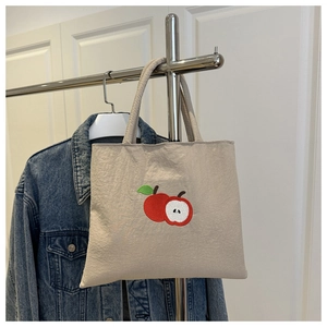 Dettaglio del ricamo a mela rossa sul materiale della borsa tote in tela beige