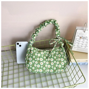 Detailed close-up of a green floral shoulder bag with a ruffled handle and bow detail