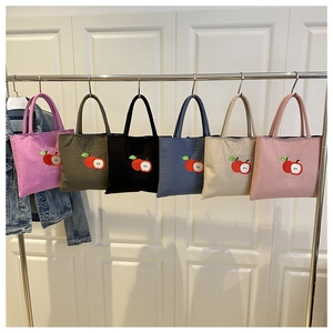 Detailed view of apple embroidery on colorful nylon tote bags hanging on a metal rack