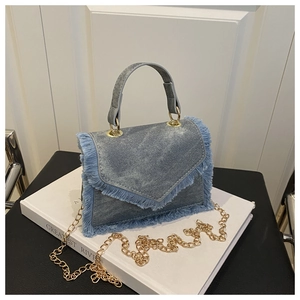 Dettaglio della borsa in denim blu lavato con bordi sfrangiati e catena dorata