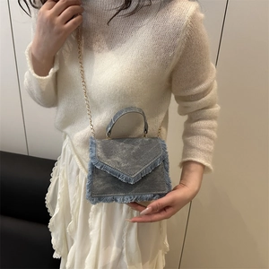 Light blue denim handbag with fringe details and gold chain strap shown on model