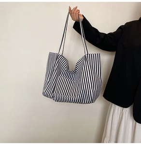 Detail of striped canvas tote bag with front pocket held by model in black blazer