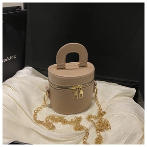 Detail of a beige cylinder handbag with gold chain strap in a black gift box packaging