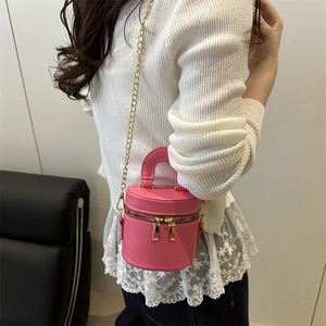 Pink mini cylinder crossbody bag with double zippers and gold chain strap on model
