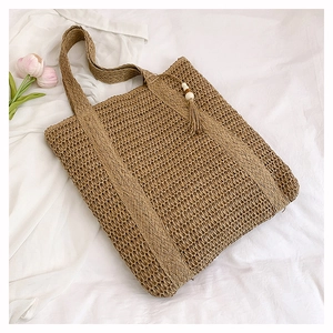 Detail of khaki straw tote bag with intricate weave, hollow structure and tassel charm