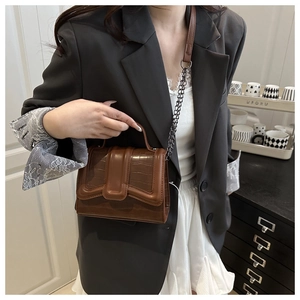 Detail of caramel crocodile embossed leather texture with sleek metal chain and handle