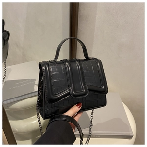 Detail of black crocodile embossed handbag showing the top handle and black metal chain strap