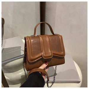 Detail of brown crocodile pattern handbag featuring metal chain and leather handle