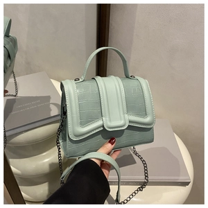 Detail of mint green crocodile embossed handbag with metal chain and top handle