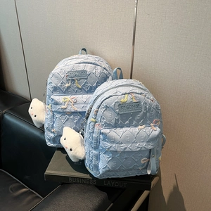 Detail of light blue nylon backpacks featuring quilted texture and bow charms with cloud pendant