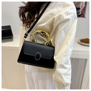 Detail of minimalist black bag showing crocodile texture flap and golden fluid handle
