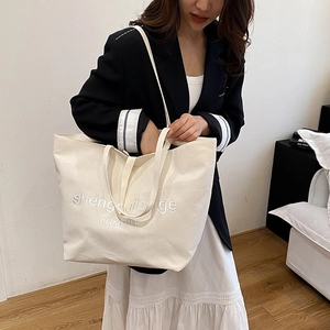 Large beige canvas tote bag with embroidered letters shown on a model for daily use