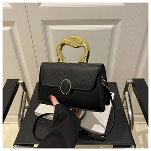 Detail of black structured handbag featuring unique gold metal handle and woven texture flap