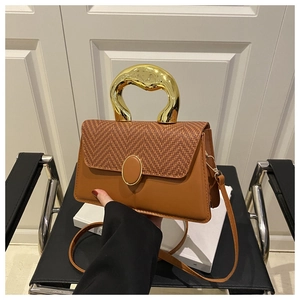 Detail of a brown woven crossbody bag with a unique irregular curved gold metal handle