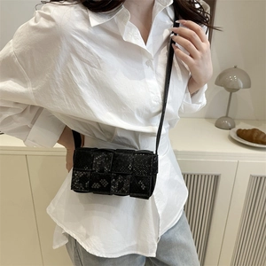 Fashionable black snake-pattern woven crossbody bag worn by a model in a minimal indoor setting