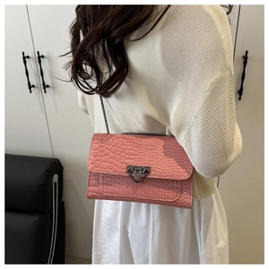 Detail view of pink crocodile-embossed chain bag worn cross-body by a model