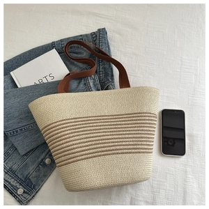 Detailed view of striped woven straw tote bag with brown handles and beige fabric texture