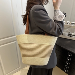 Striped woven straw tote bag with brown straps shown from a stylish side view angle