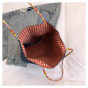 Dettaglio della borsa in denim con manici intrecciati colorati e fodera a scacchi
