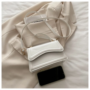 Detail of white structured handbag with wavy flap and gold lock on beige blazer
