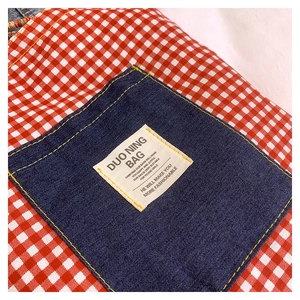 Dettaglio del tessuto a quadri rossi con tasca in denim e cuciture gialle sulla borsa