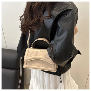Close-up of a cream crossbody bag worn with a black leather jacket and white skirt