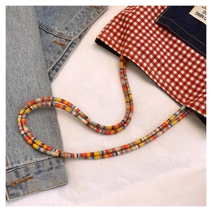 Dettaglio borsa a quadretti rossi con tasca in denim e tracolla colorata di perline