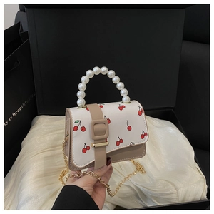 Detail of white mini bag with cherry print, pearl handle, and golden metal chain strap