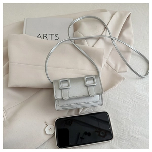 Detailed close-up of mini silver crossbody bag with dual square buckles on beige fabric