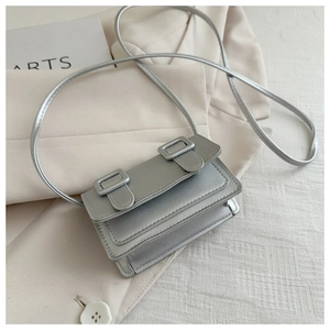 Macro shot of a silver metallic mini crossbody bag with double buckles on a beige suit