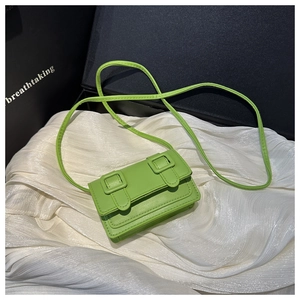 Detail of lime green mini crossbody bag with double buckle straps on white silk fabric