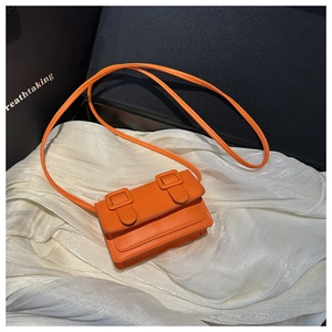 Detail shot of mini orange crossbody bag with decorative buckles and fine leather texture