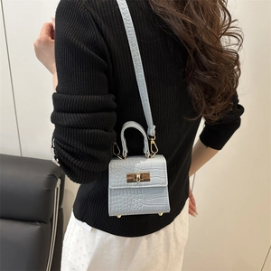 Light blue faux crocodile skin mini handbag with gold metal clasp on model shoulder