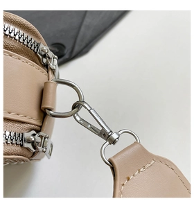 Detailed view of silver metal hooks and double zippers on a beige leather crossbody bag