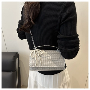 Detail of silver woven handbag featuring a pearl bow charm and round metal handle