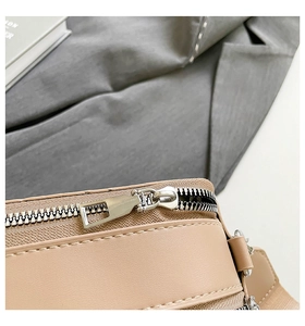 Detailed close-up of smooth beige leather stitching and silver metal zipper on the square bag